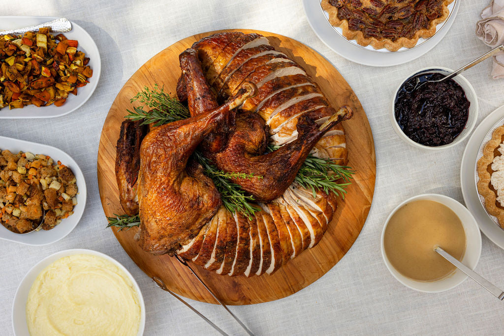 Thanksgiving dinner spread: carved turkey, stuffing, potatoes, roasted vegetables, cranberry compote, gravy and pie